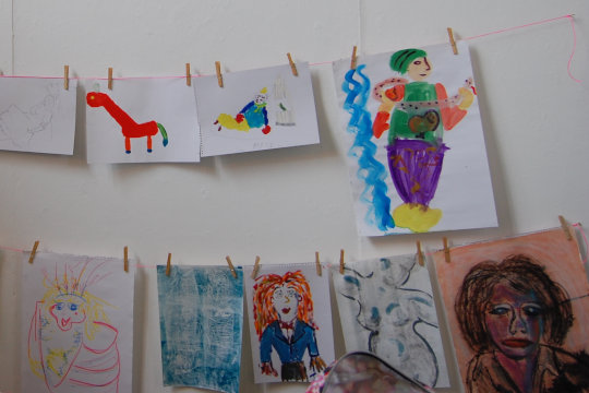 Rows of drawings and paintings hanging from washing lines. The works were made by people participating in our popular 'Dress, Paint and Pose like a Dandy' workshop. People can rummage through our hand-made costumes and be a model, and they can also draw or paint other models.