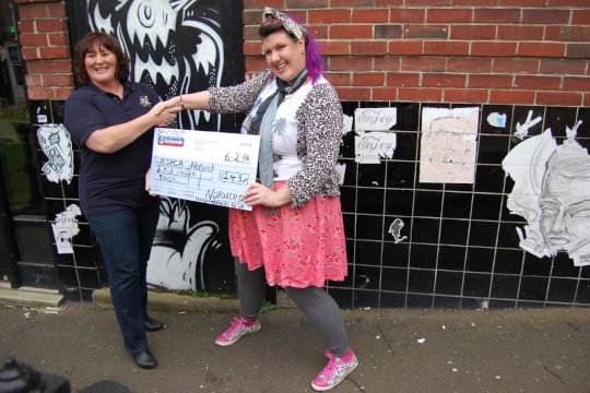 Dandy Christina Sabberton flamboyantly presenting a large cheque for £243 to the RSPCA from the sales of bird paintings at the Birdcage pub. The photo was taken outside the pub.