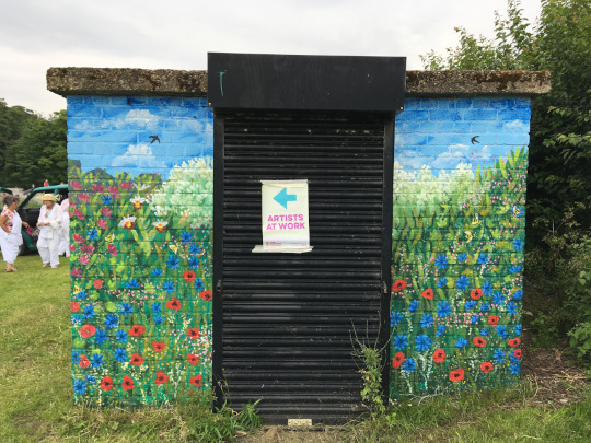 The painted right side of the building, with lots of flowers and a metal shutter door with an Artists At Work sign.