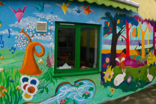 Here we see the very nearly finished full mural. Dugald is just putting a finishing touch to the top very left hand corner of the mural. The mural covers one full wall of the kid’s outdoor courtyard lunchtime play area. The theme for the mural chosen by the Hamlet Charity was musical meadows so the dandies painted a whimsical meadow scene with instruments and flowers growing all over the place. Also in the mural are ideas offered from the kids and staff that are also reflected in other areas around the Hamlet Centre. The dandies painted honey Bees gathering nectar all over the mural just like they have set up in their sensory room. Origami birds are painted flying in the sky up the top which is reflected from the hanging decorations in the reception of a thousand paper cranes inspired by the Japanese kids story.