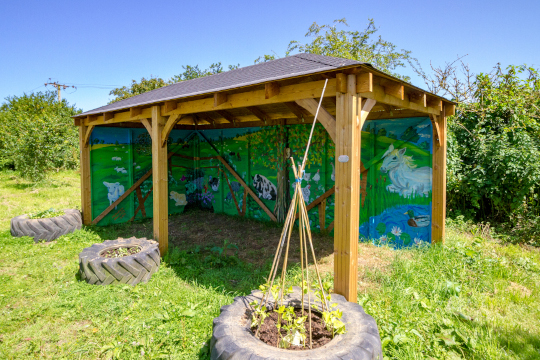The finished mural. It is painted on the inside of a wooden shelter used by volunteers and visitors. The mural features a landscape with trees, a pond and animals found on the farm.