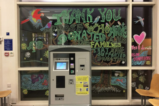 A chalked message on one of the windows that thanks those who have donated organs. There is a parking ticket machine in the foreground.